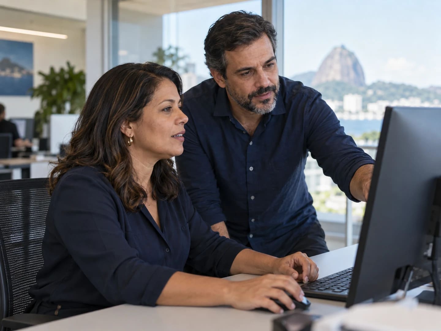 Dois profissionais analisam informações em uma tela.