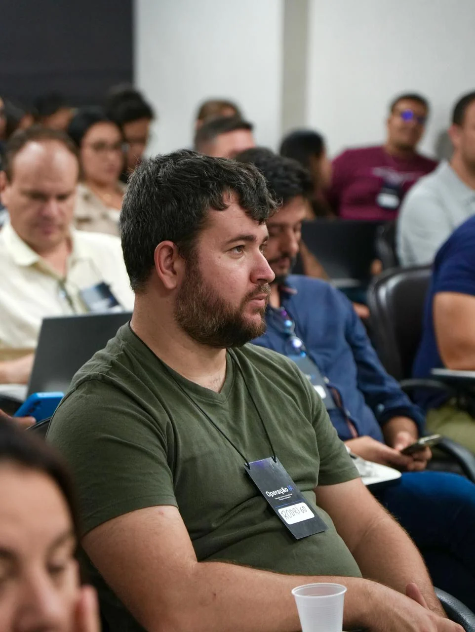 Participante atento durante a primeira edição da Operação IA, com outras pessoas e notebooks ao fundo.